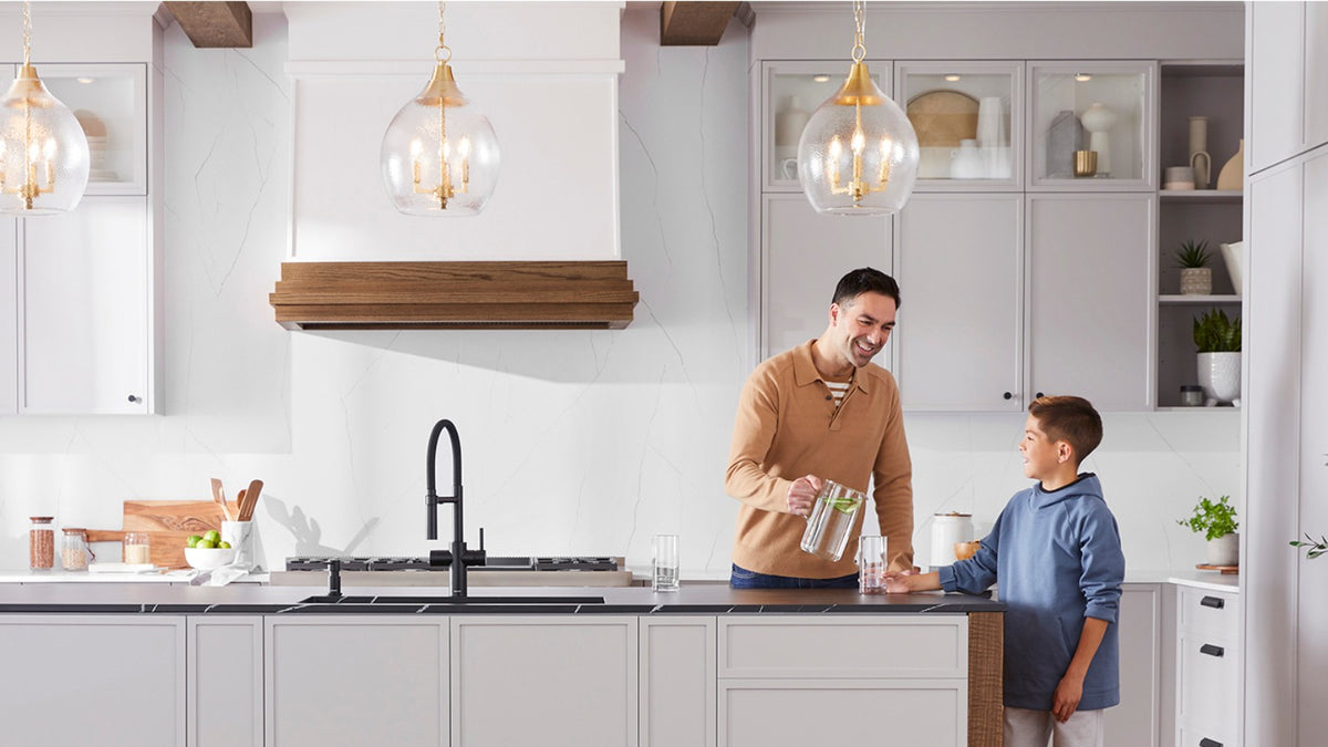 A father and son enjoying filtered water in their kitchen, featuring a Blanco Catris Flexo Filter faucet installed in a dark kitchen island
