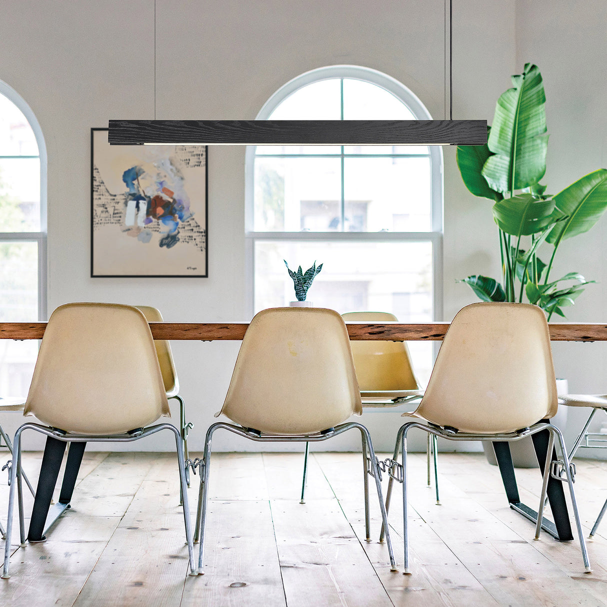Beige chairs around a wooden dining table with a plant and artwork in the background.