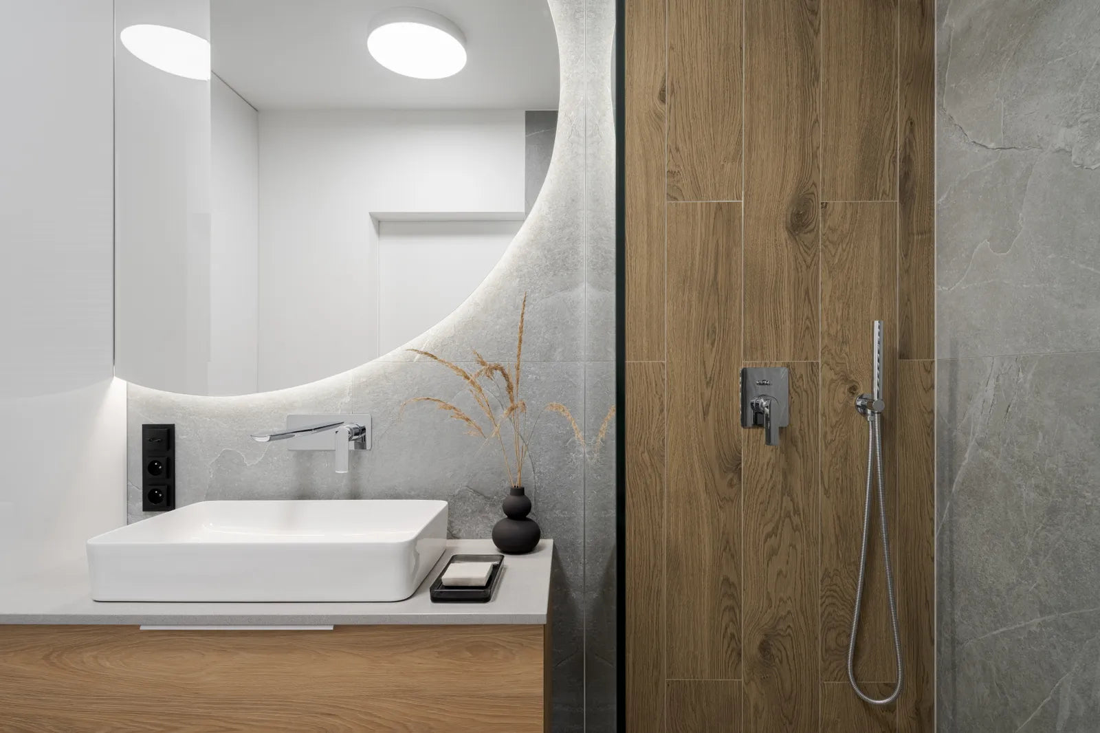 Modern bathroom with recessed ceiling lights over a glass shower enclosure and sconces beside the vanity mirror