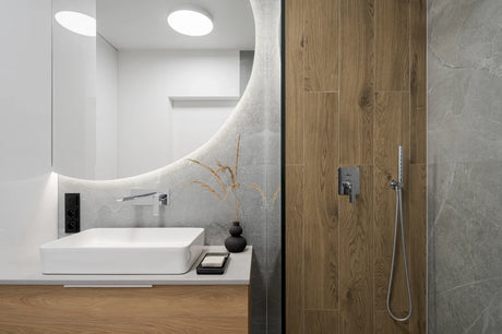 Modern bathroom with recessed ceiling lights over a glass shower enclosure and sconces beside the vanity mirror