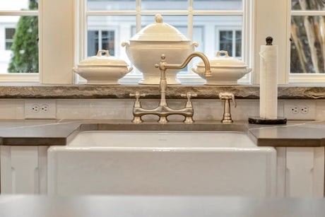Polished nickel bridge faucet with twin handles mounted behind a white farmhouse sink in a classic kitchen