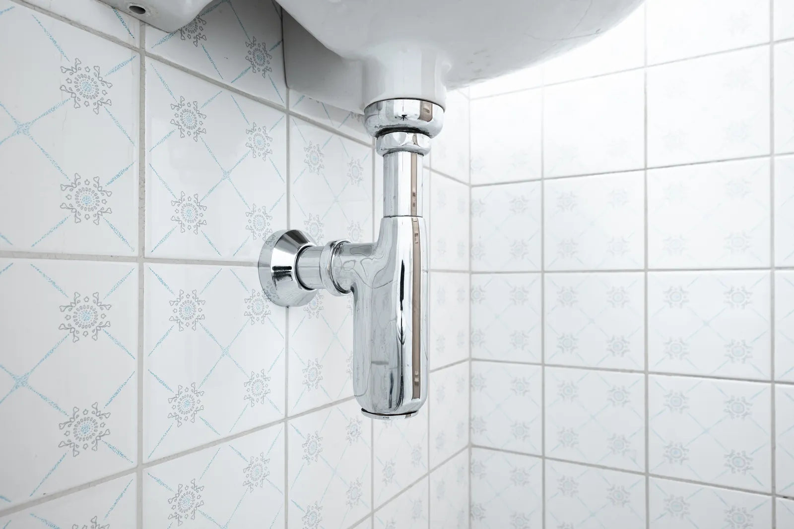 Polished chrome bottle trap and supply lines beneath a wall-hung bathroom basin