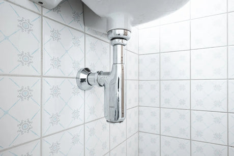 Polished chrome bottle trap and supply lines beneath a wall-hung bathroom basin