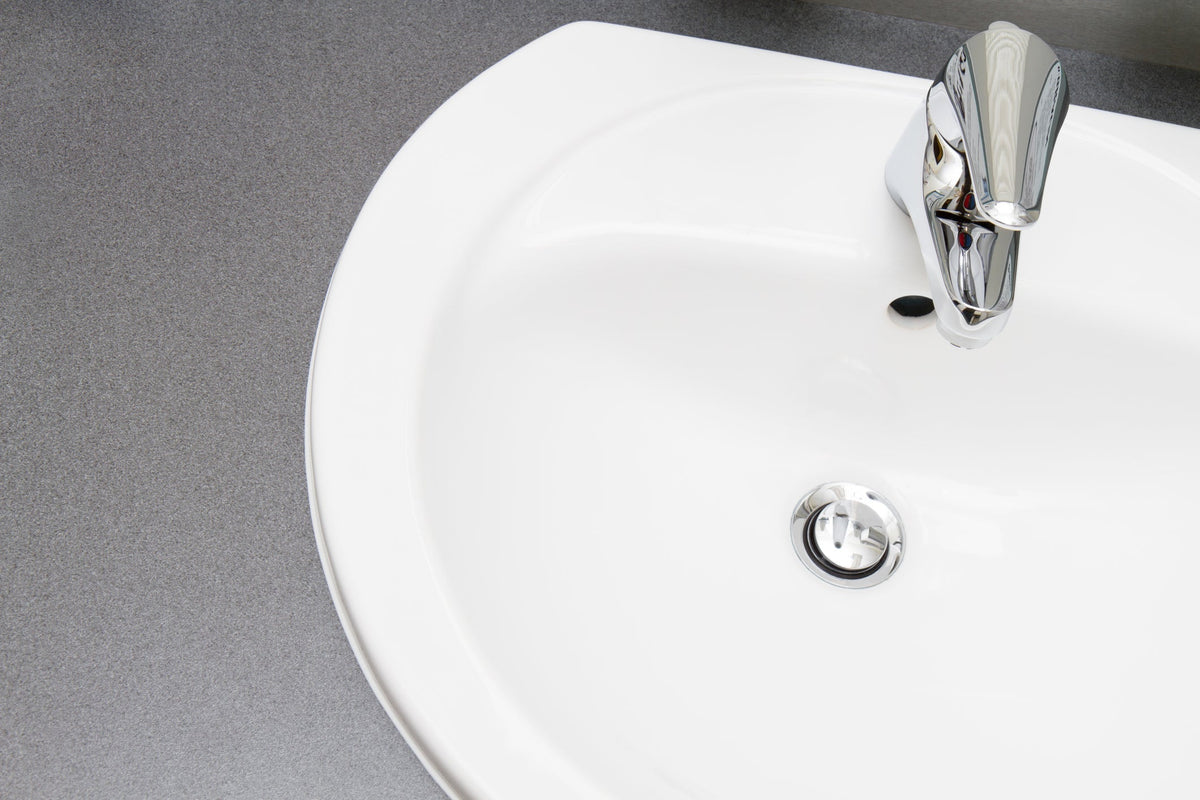 Hand lifting a metal pop-up stopper out of a bathroom sink drain to clean away hair and soap buildup