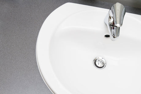 Hand lifting a metal pop-up stopper out of a bathroom sink drain to clean away hair and soap buildup