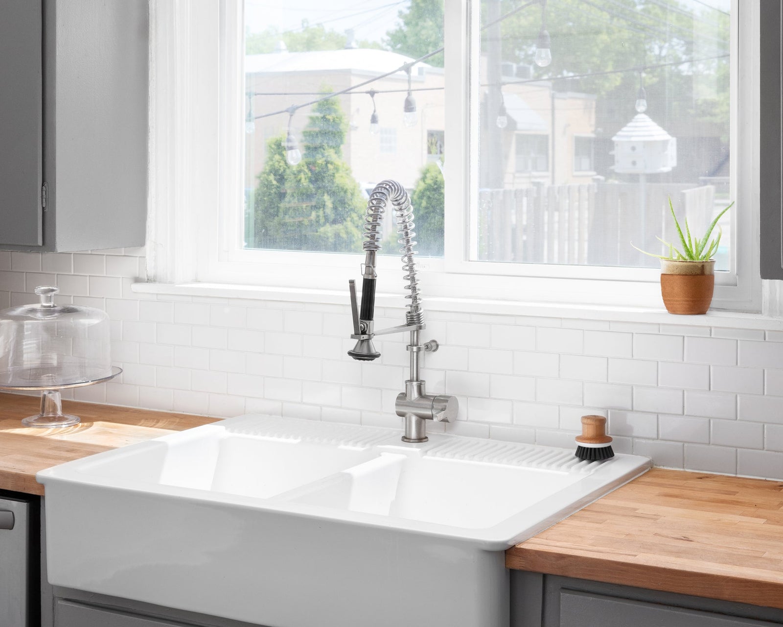 White apron-front farmhouse sink with a bridge faucet and open wood shelving in a modern farmhouse kitchen