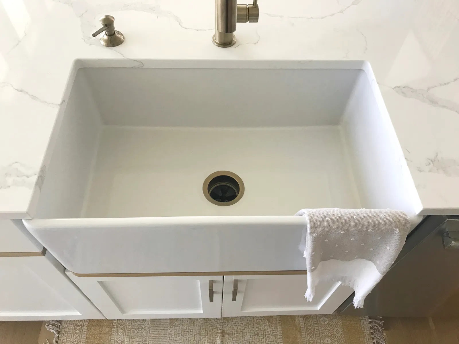 White fireclay farmhouse apron-front sink in a bright kitchen with a brass bridge faucet