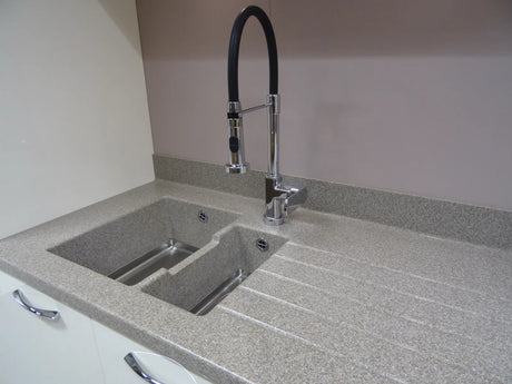Dark granite composite kitchen sink with faucet set into a stone countertop in a modern kitchen