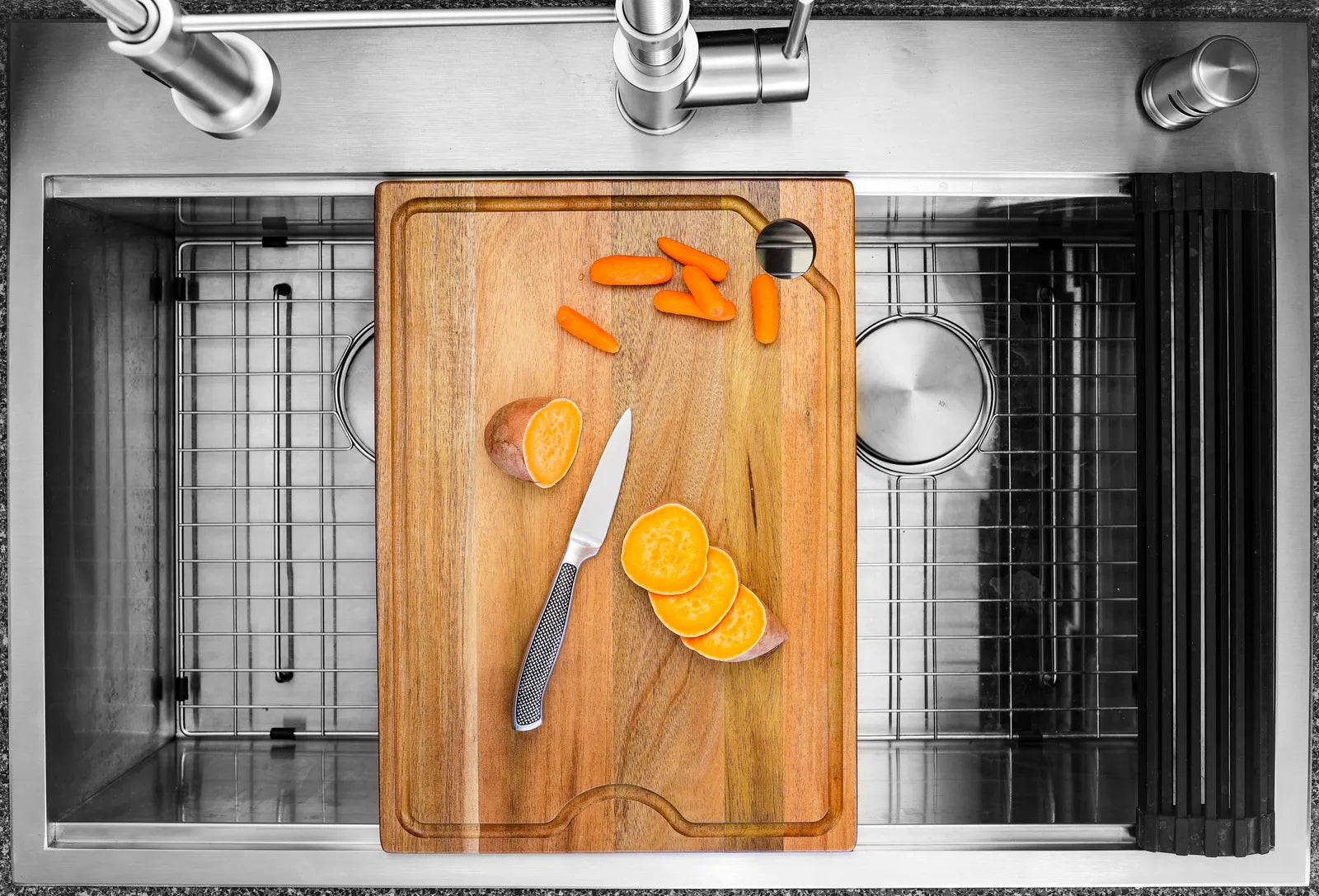 Stainless steel workstation kitchen sink with a wood cutting board sliding on its integrated ledge