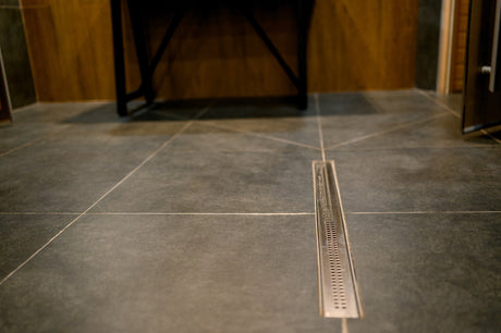 Stainless steel linear shower drain set into a tiled walk-in shower floor