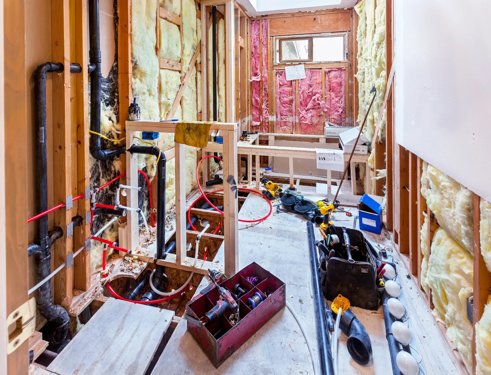 Bathroom under renovation with exposed wall framing and rough plumbing lines before drywall