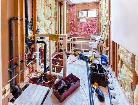 Bathroom under renovation with exposed wall framing and rough plumbing lines before drywall