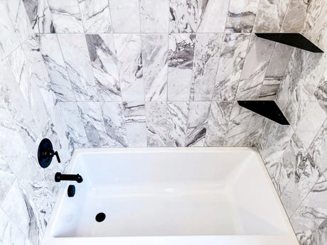 White alcove bathtub with a tile surround installed between three walls in a renovated bathroom