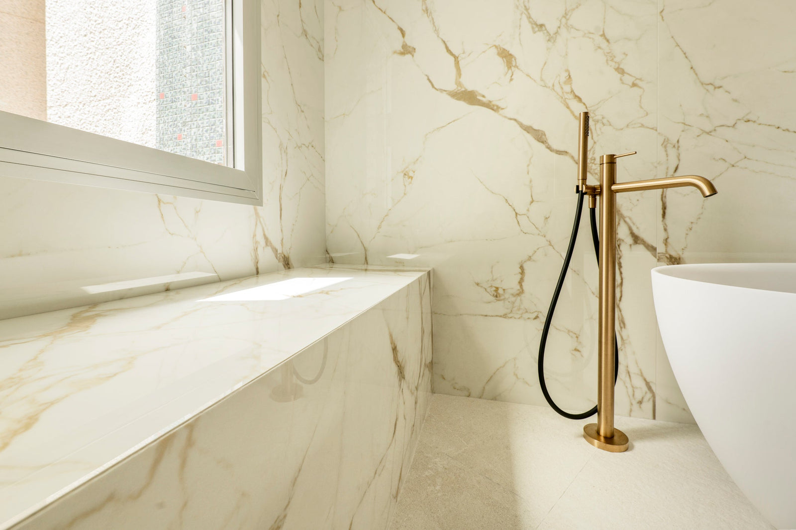 Floor-mount tub filler standing beside a freestanding bathtub in a bright modern bathroom