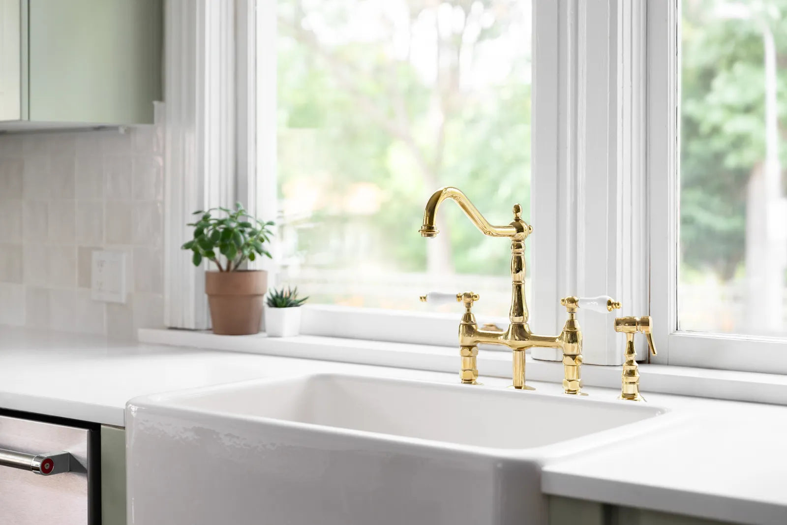 Traditional two-handle bridge faucet in a warm metal finish mounted over a white farmhouse kitchen sink