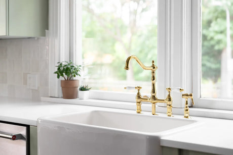 Traditional two-handle bridge faucet in a warm metal finish mounted over a white farmhouse kitchen sink