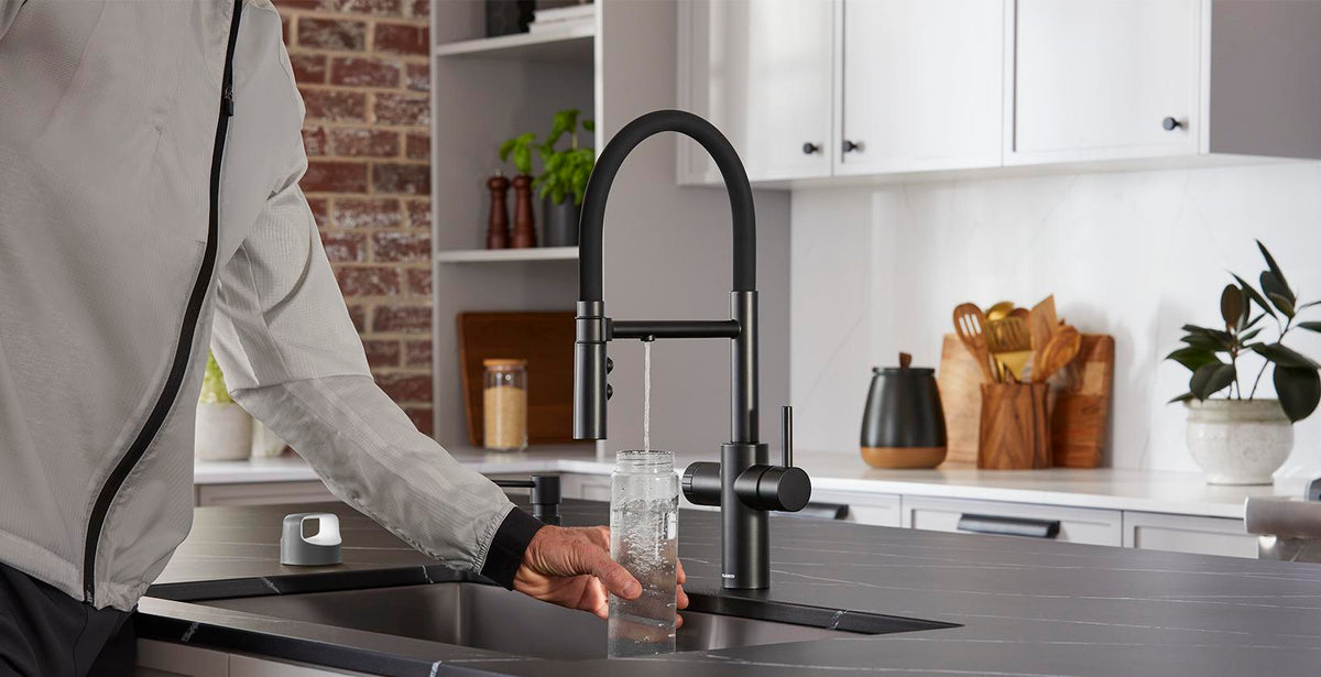 Person filling a bottle with filtered water from a Blanco Catris Flexo Filter faucet — Matte Black finish, in a modern, dark kitchen