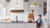 A father and son enjoying filtered water in their kitchen, featuring a Blanco Catris Flexo Filter faucet installed in a dark kitchen island
